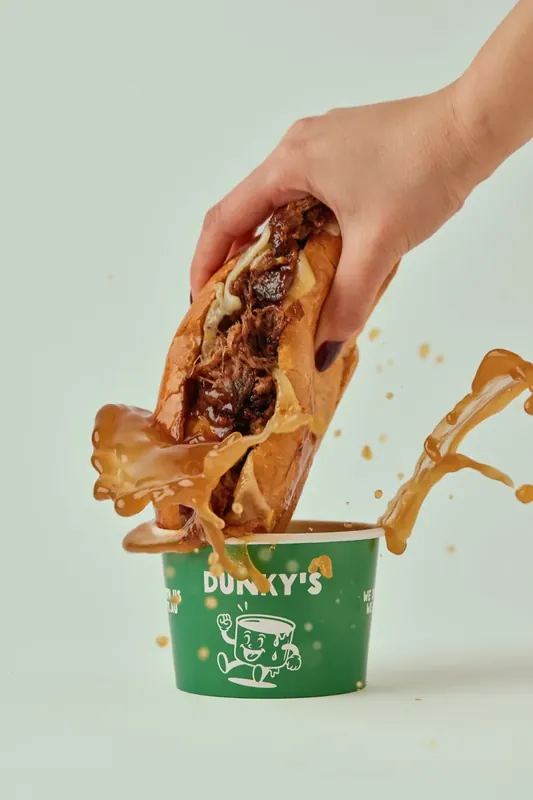 A Dunky's beef roll being dunked into a cup of rich beef jus